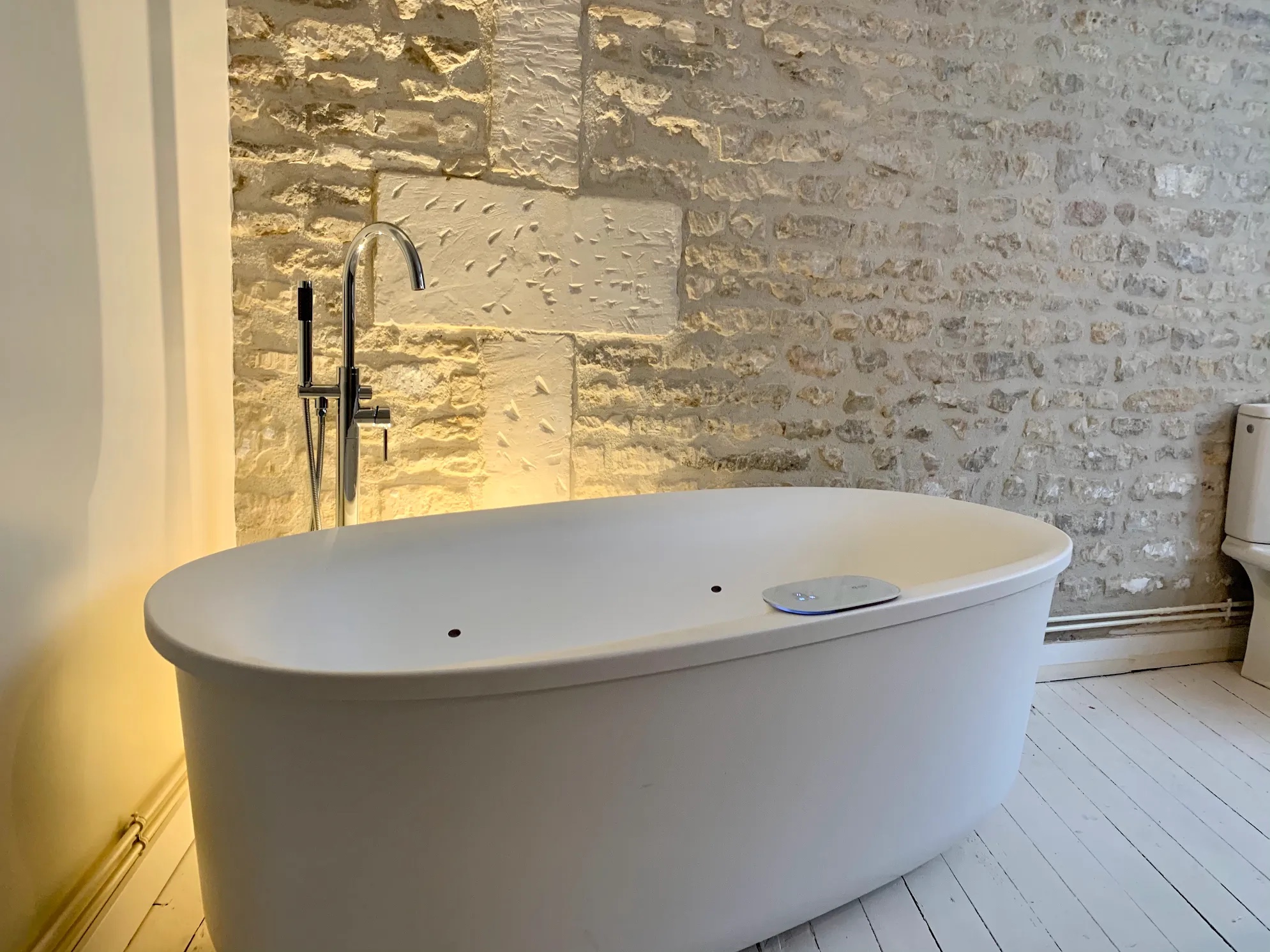 Bathroom with exposed restored stone wall, freestanding Jacuzzi bathtub, and custom floor lighting