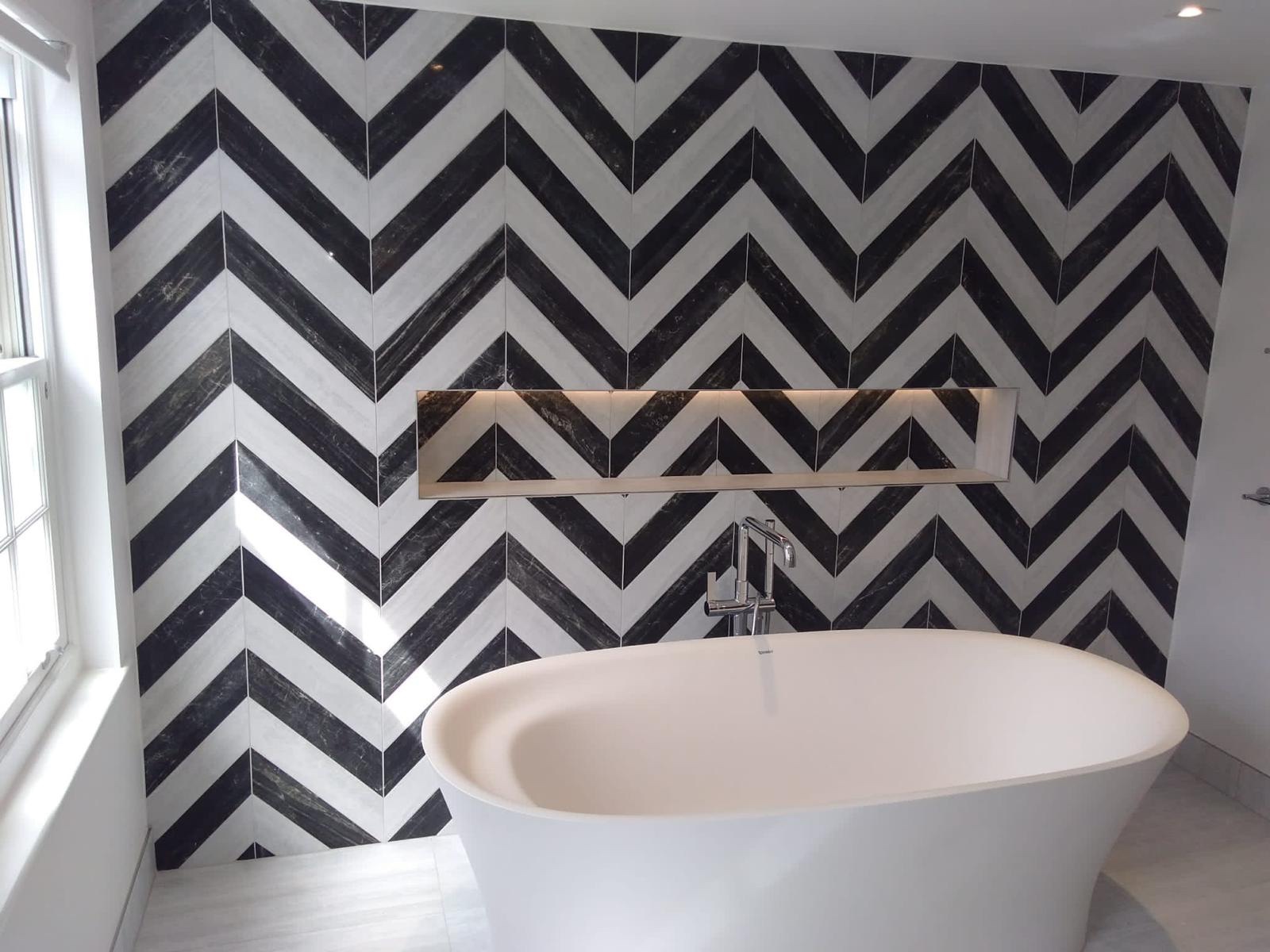 Bathroom renovation with bold black and white chevron tile pattern, freestanding bathtub, and recessed LED niche