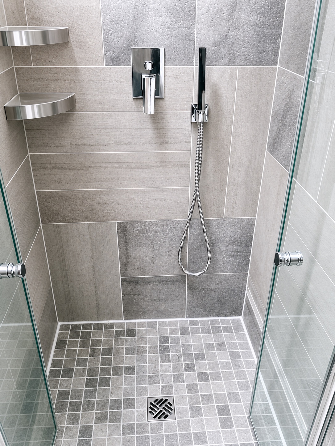 New loft shower room with grey large-format tiling, mosaic floor, and chrome fittings